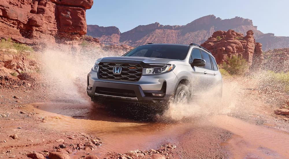 White 2025 Honda Passport Trailsport driving off-road over a shallow pond.