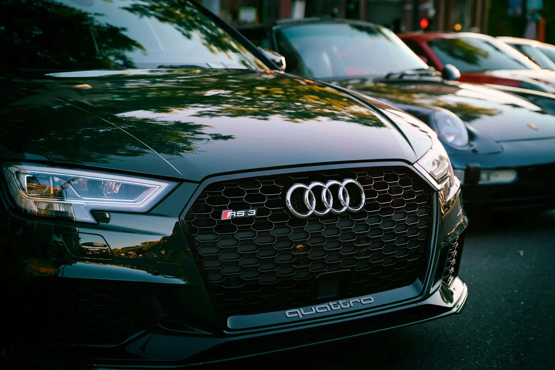 Close-up of a blue Audi RS3 grille showing the honeycomb mesh insert, quattro badge, and illuminated ring emblem