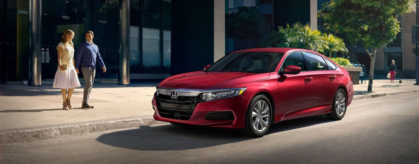 A couple is walking toward a red 2021 Honda Accord Touring 2.0T on a city street after leaving a Rochester Honda Accord dealer.
