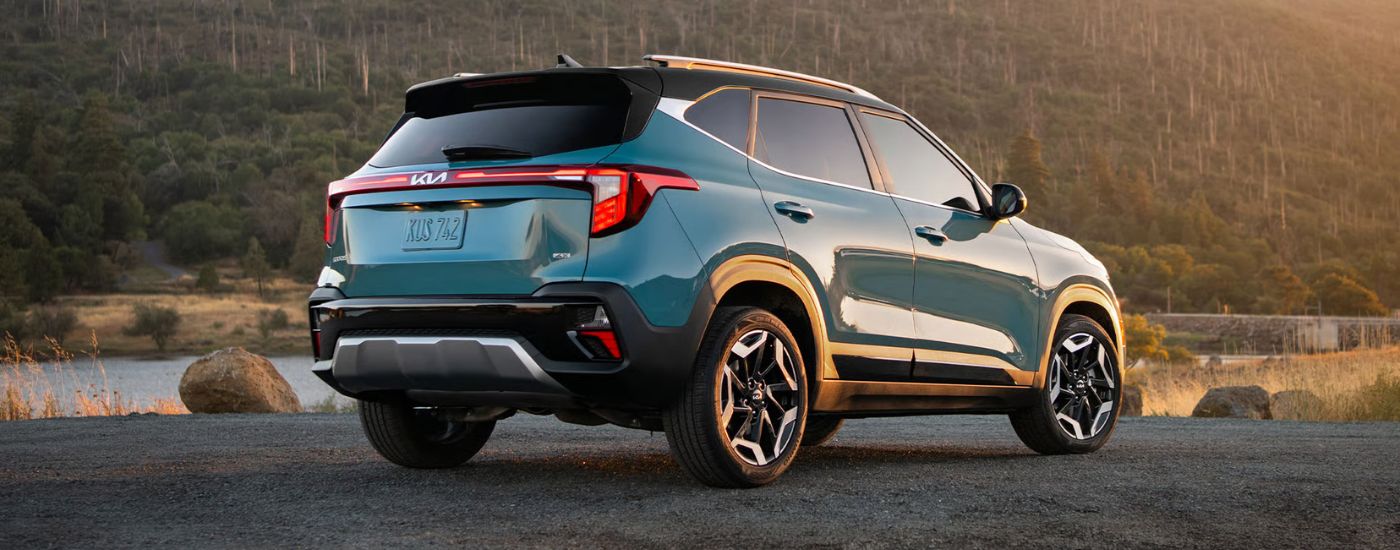 Rear view of a blue 2026 Kia Seltos parked by a river at sunset.