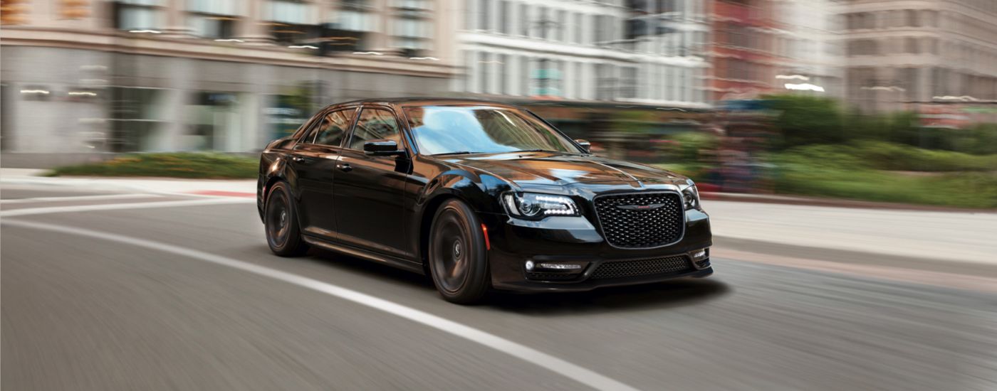 A black 2022 Chrysler 300 is shown driving on a city street after leaving a used Chrysler dealer.