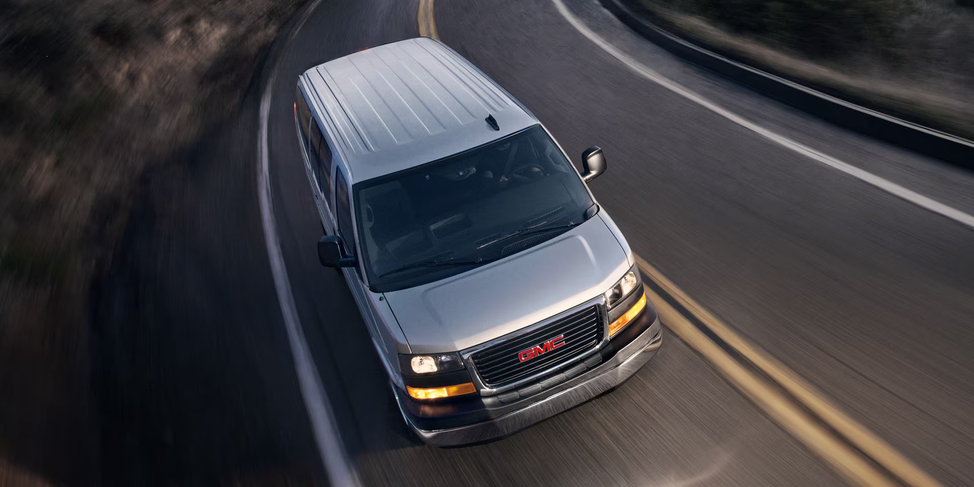 Silver GMC Savana driving on a winding road