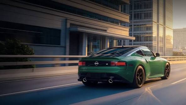 2027 Nissan Z in green driving on a city street, rear three-quarter view