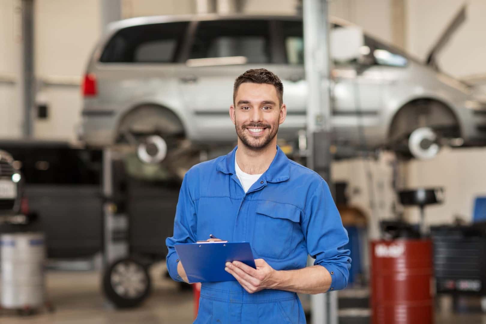 Vehicle service technician holding clipboard standing in front of lifted vehicle