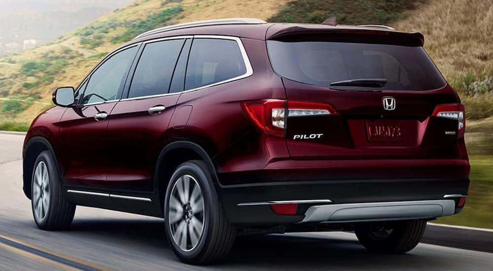A red 2021 Honda Pilot Touring is shown from the rear driving down an open road.