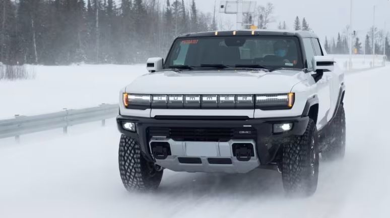 white Hummer EV driving down snow covered road during a winter snow storm