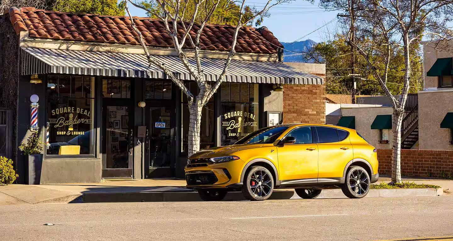 A yelloe SUV parked infront of a barber shop.