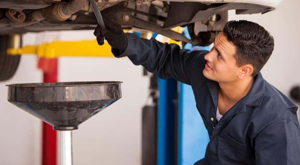 A mechanic is shown performing an oil change under a vehicle.