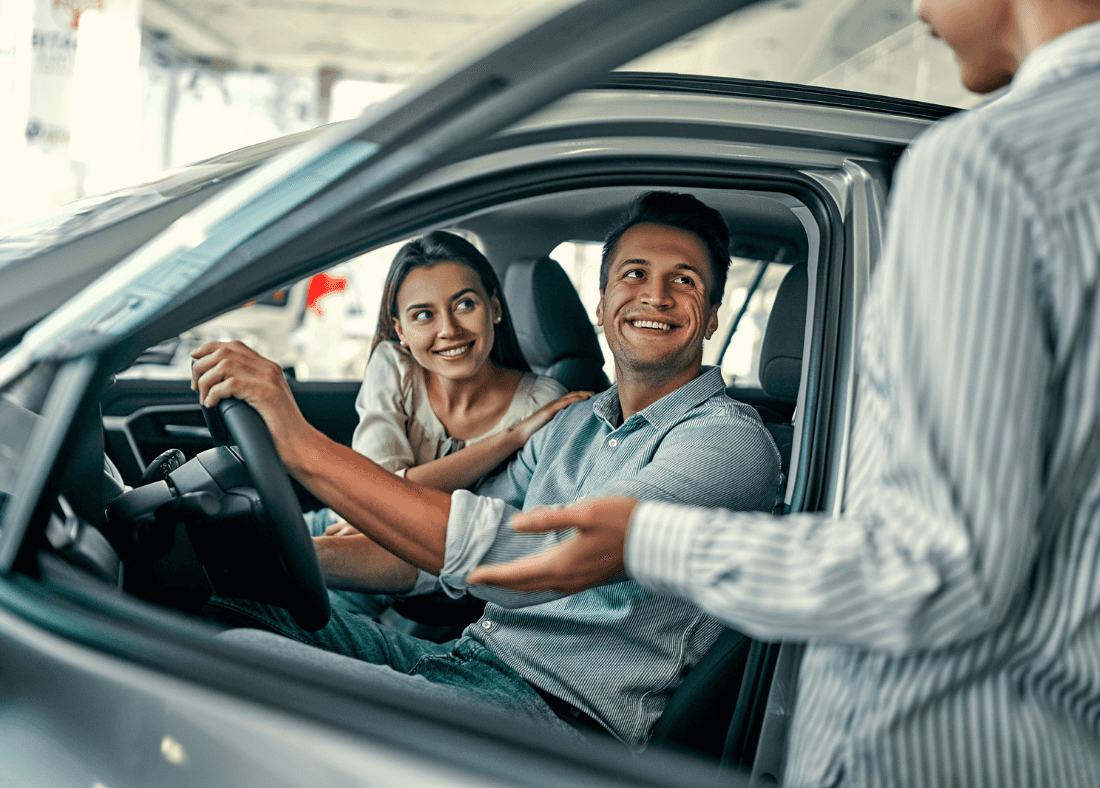Couple inside a Kia vehicle smiling and engaging with a sales representative at Kiefer Kia dealership, highlighting a friendly car-buying experience.