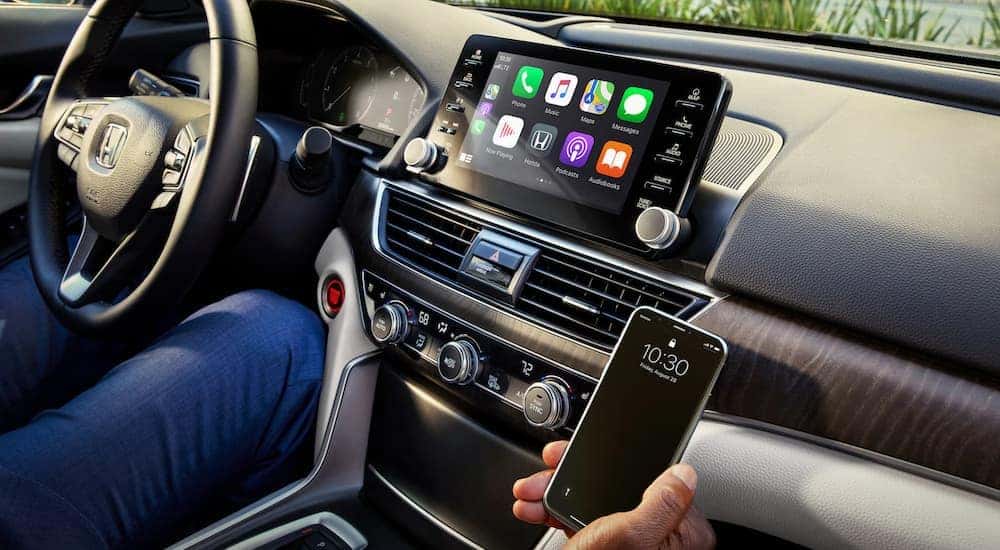 The infotainment screen is shown behind a phone inside a 2021 Honda Accord Touring.