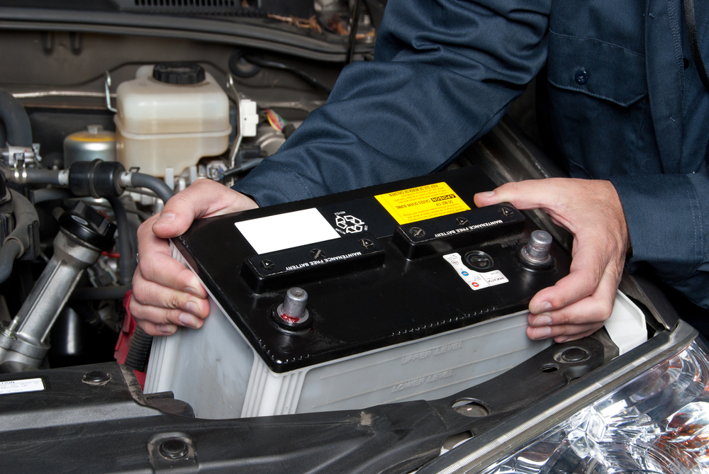 Blue Shirt wearing Mechanics hands are putting a car battery into a cars engine