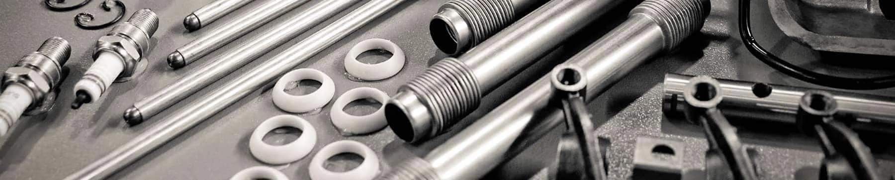 Nissan engine parts including spark plugs, valves and gaskets laid out on a dark workbench