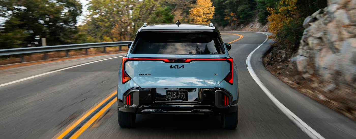 Rear of a blue 2027 Kia Seltos driving down a road.