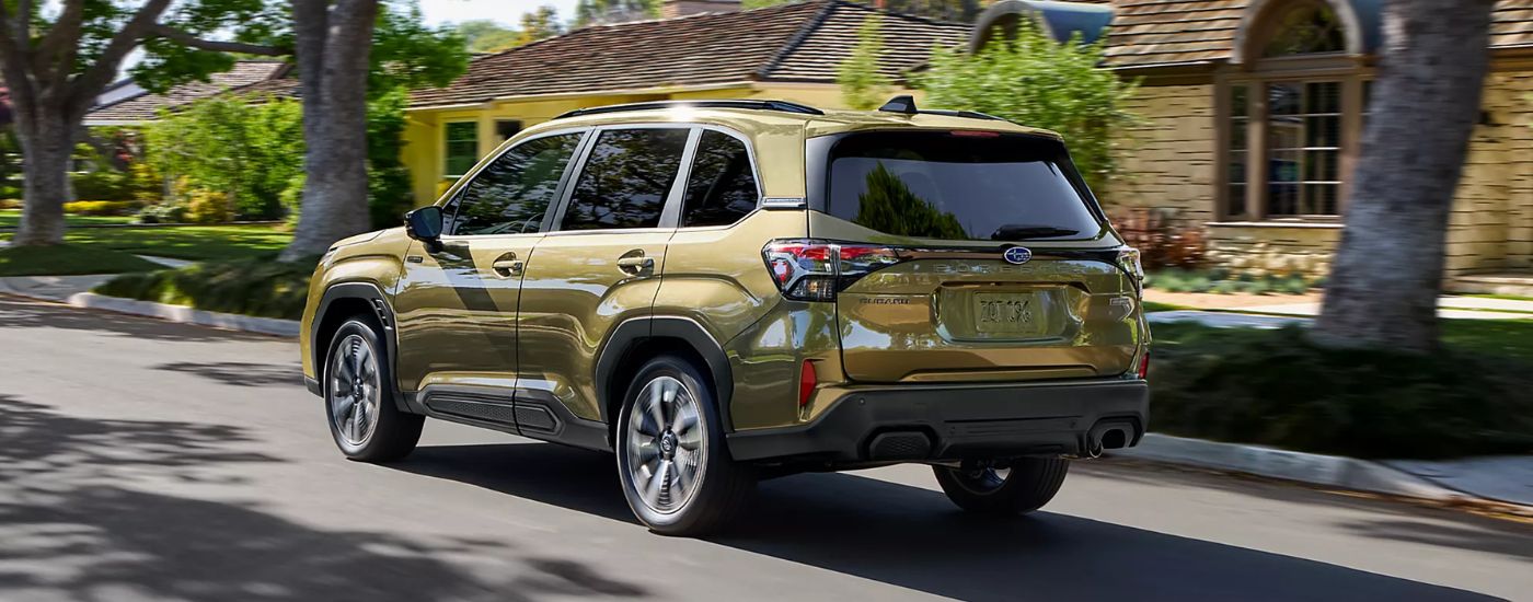 A green 2026 Subaru Forester Touring Hybrid driving by houses.