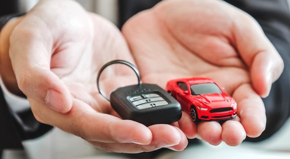 Hands holding a car key and red toy car at a dealership