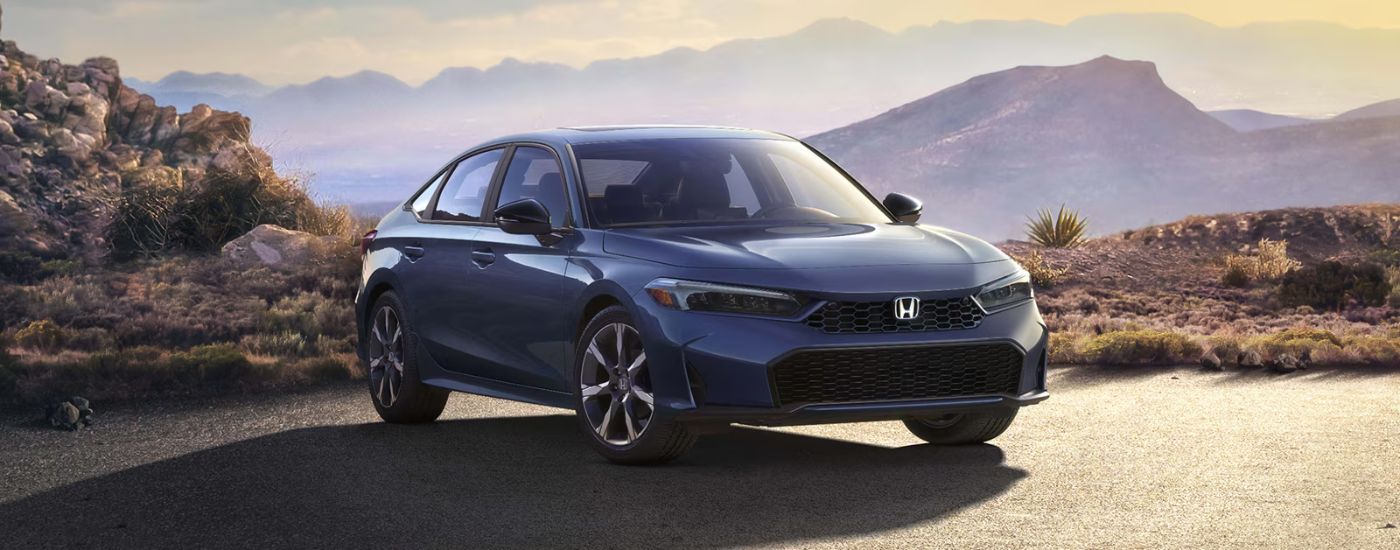 A blue 2026 Honda Civic Sport Touring Hybrid parked in front of mountains.
