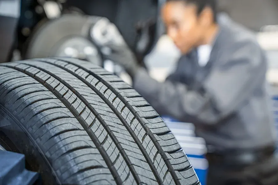 Close-up of tire tread in the foreground, with a technician working on a wheel and brake components in the blurred background