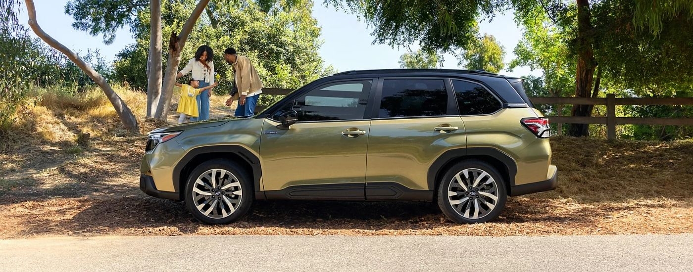 A green 2025 Subaru Forester Hybrid parked near a family.