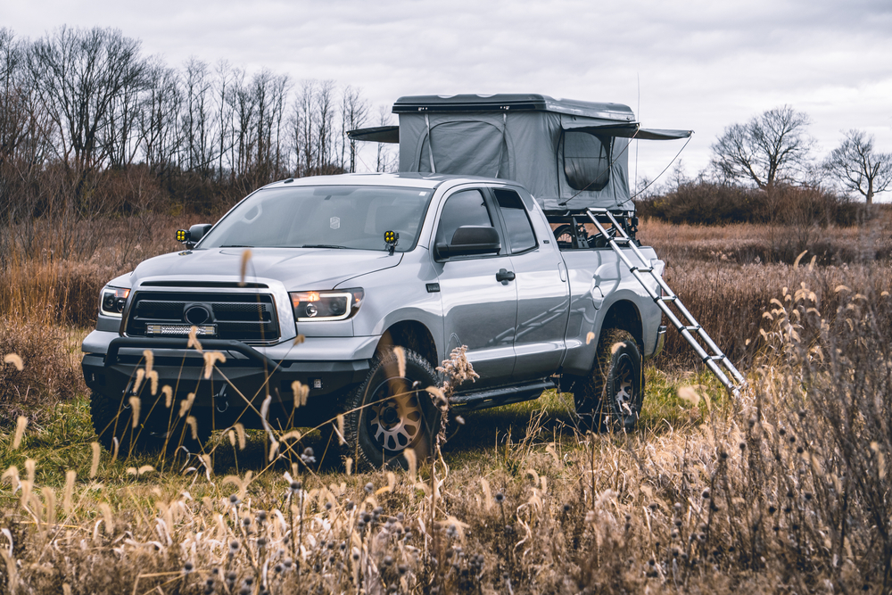 silver pickup truck with a truck bed tent, parked in a field