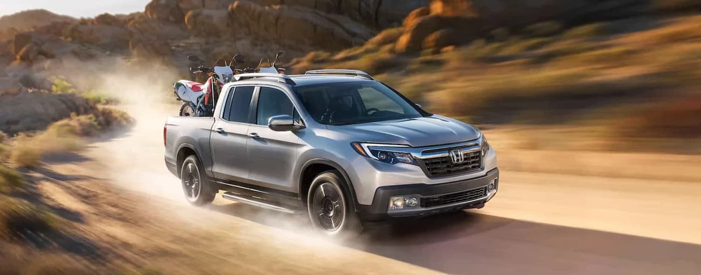 A silver 2020 Honda Ridgeline RTL-E is shown driving on a dusty road.