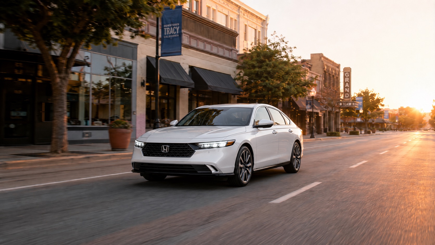 A white 2026 Honda Accord driving through Downtown Tracy California at sunrise, highlighting its modern design and sleek LED headlights against historic storefronts.