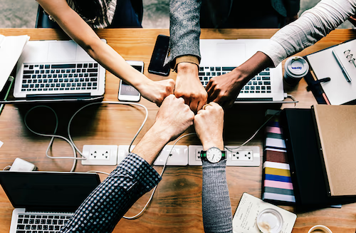 Team members bumping fists over a table of laptops
