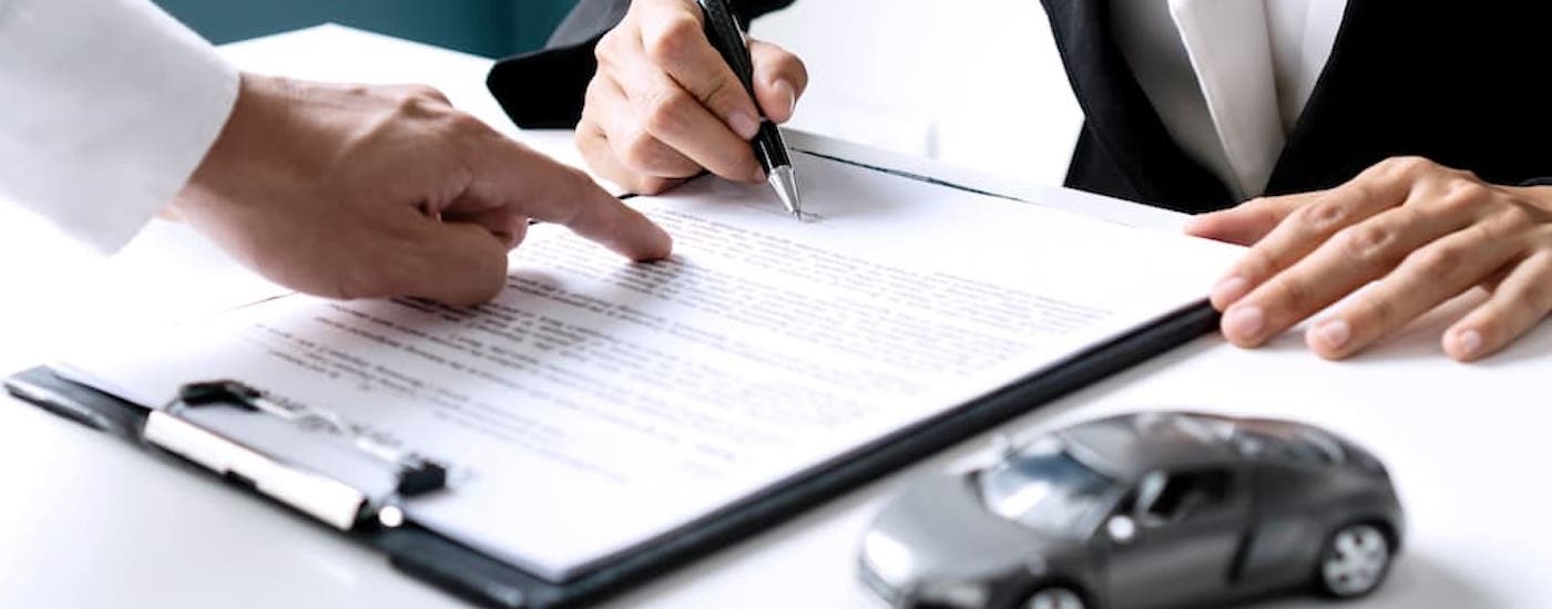 Close-up of a person signing a lease at a car dealership.