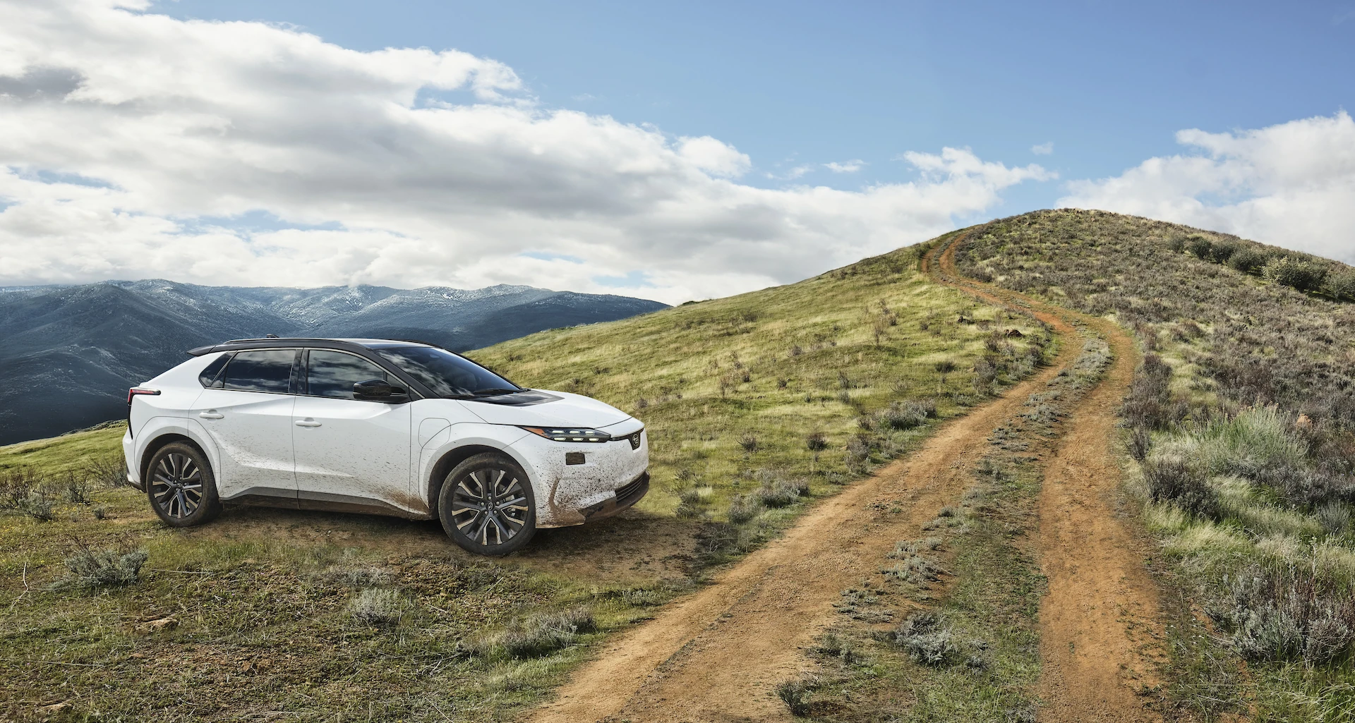 A static image of a white 2027 Subaru Solterra parked on a grassy hill.