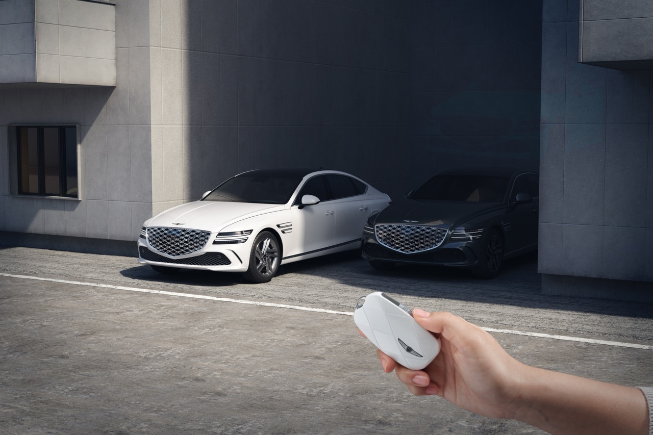 Genesis G80 in Uyuni White parked beside black G80, remote key in foreground near modern garage