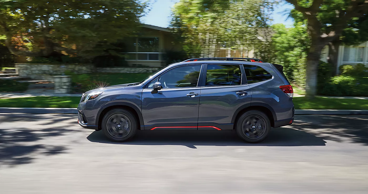 Gray 2024 Subaru Forester Sport with orange trim driving down a tree-lined street