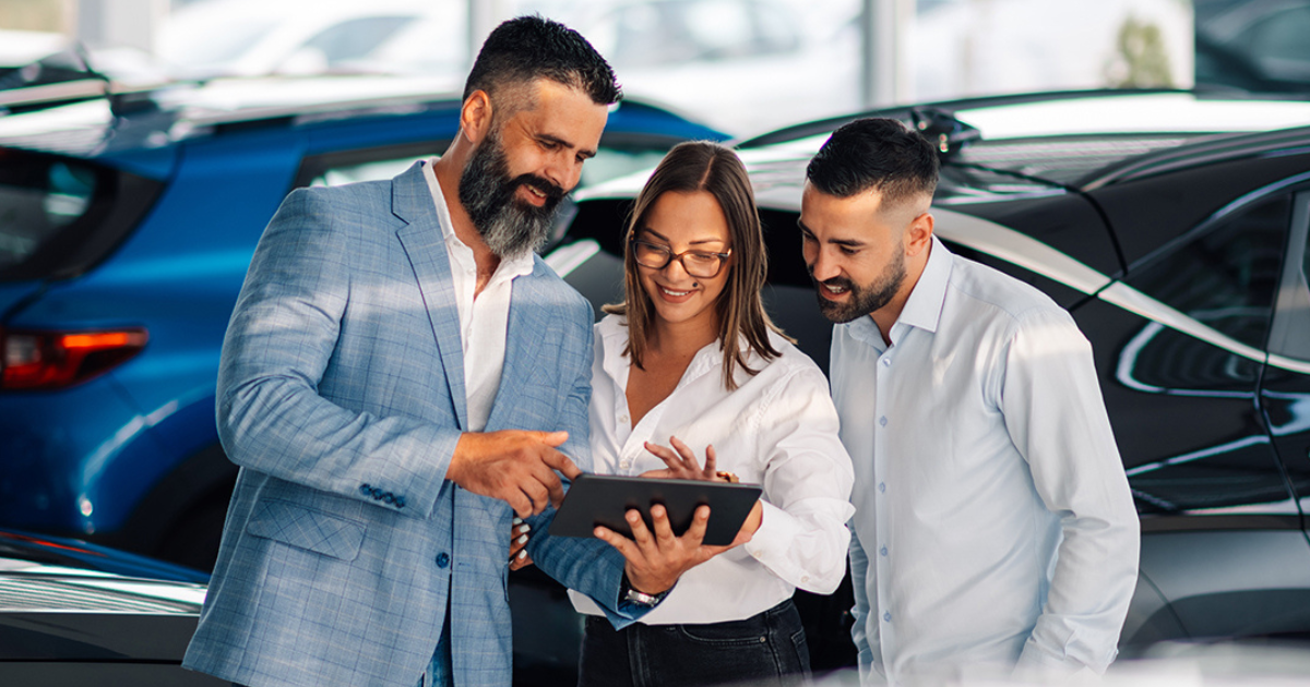 Customers and a sales associate look at a tablet in a vehicle showroom