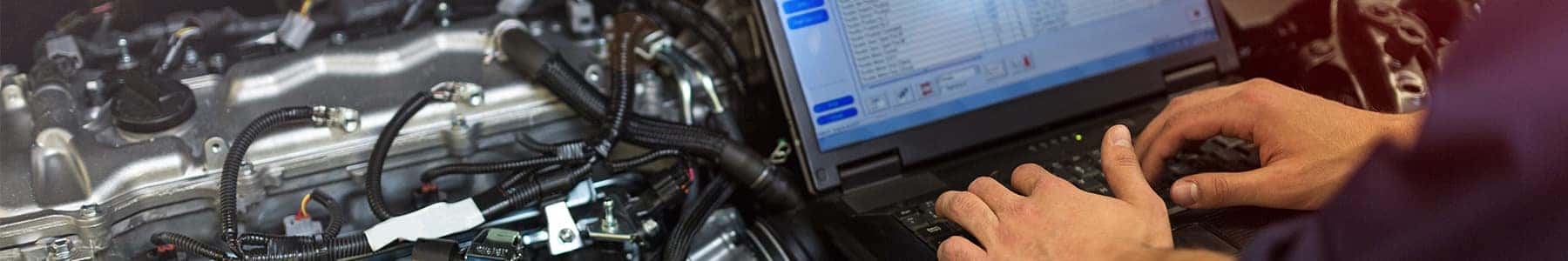Technician running a diagnostic scan on a laptop beside an open engine bay