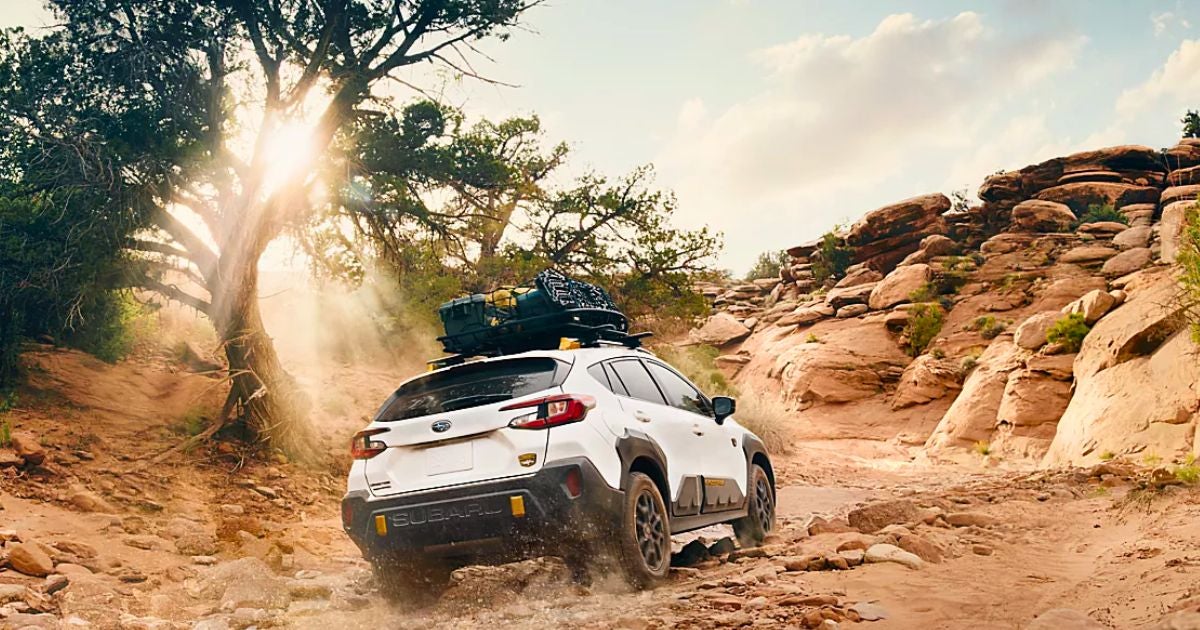 White Subaru Crosstrek Wilderness with a roof basket climbing a rocky desert trail