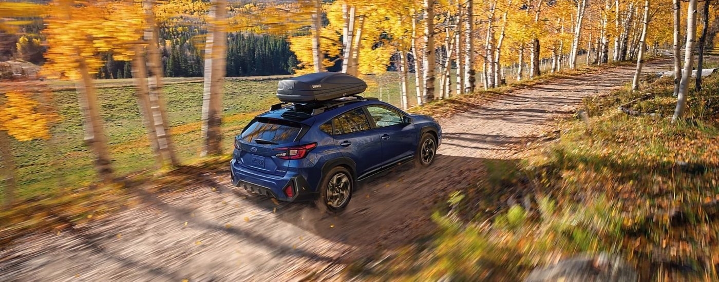 Blue 2024 Subaru Crosstrek driving on a tree-lined trail.
