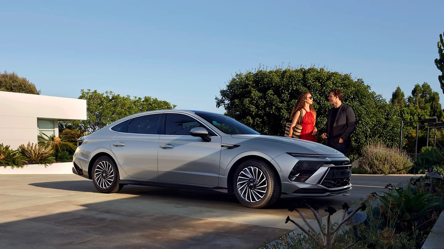 A man and woman standing next to a gray car.