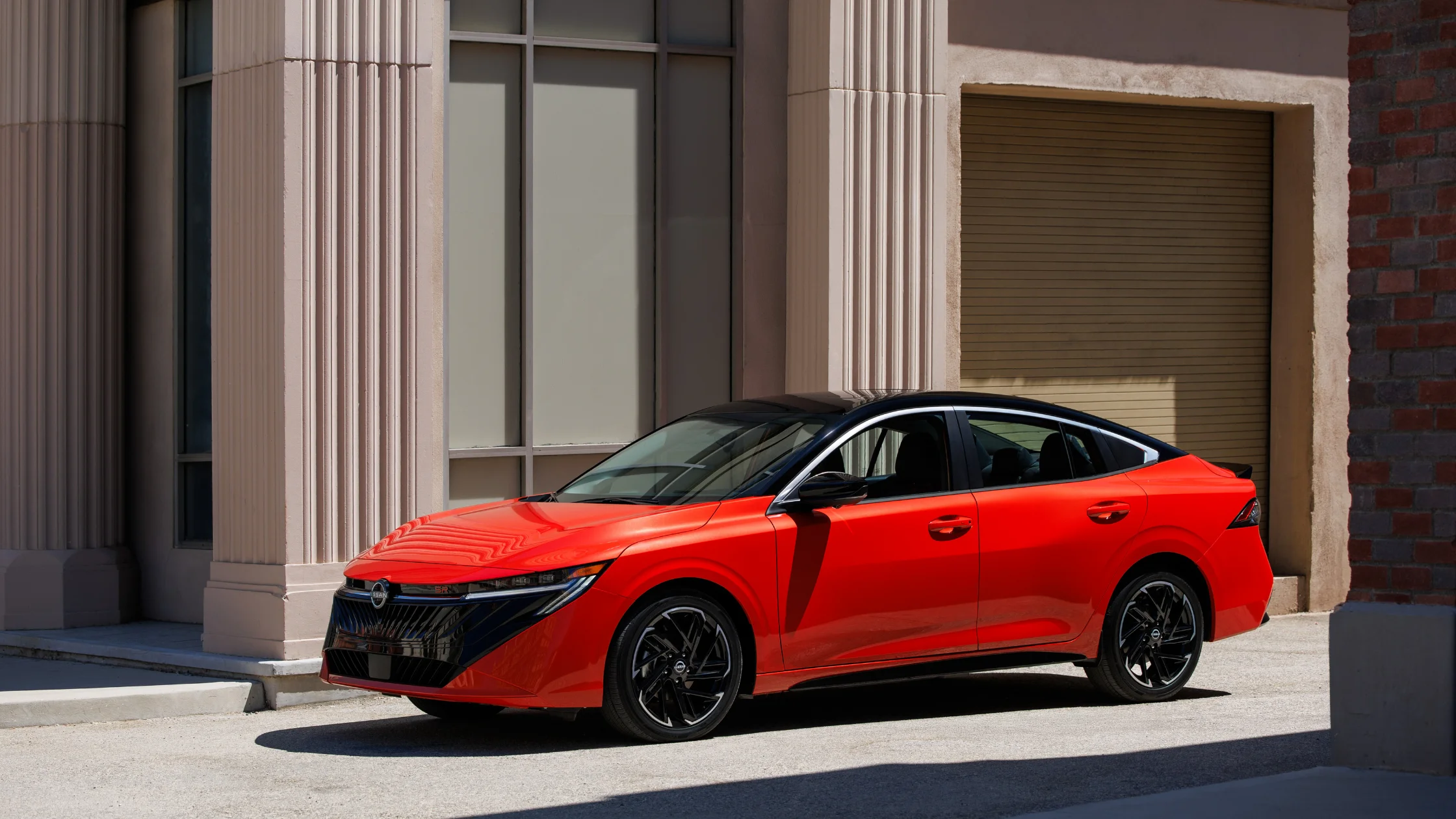 2025 Nissan Sentra® red sedan parked beside modern building with black roof and wheels