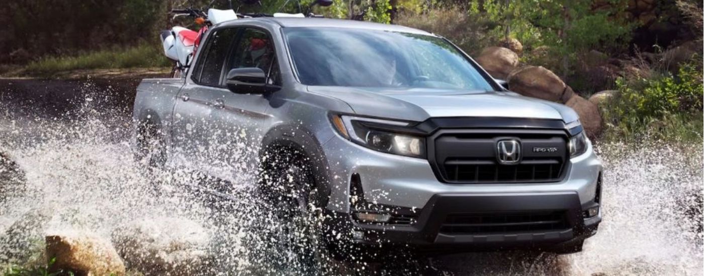 A silver 2026 Honda Ridgeline shown driving through water.