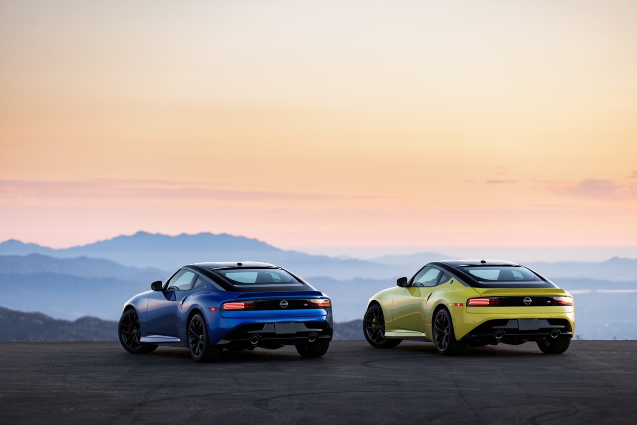 Two Nissan Zs, blue and yellow, on a mountain at sunset