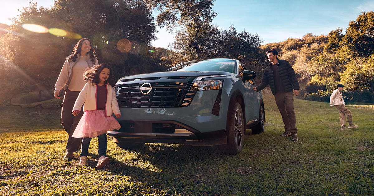 A Nissan Pathfinder mid-size SUV, featuring a bold front grille and a light blue exterior finish in a scenic outdoor setting.