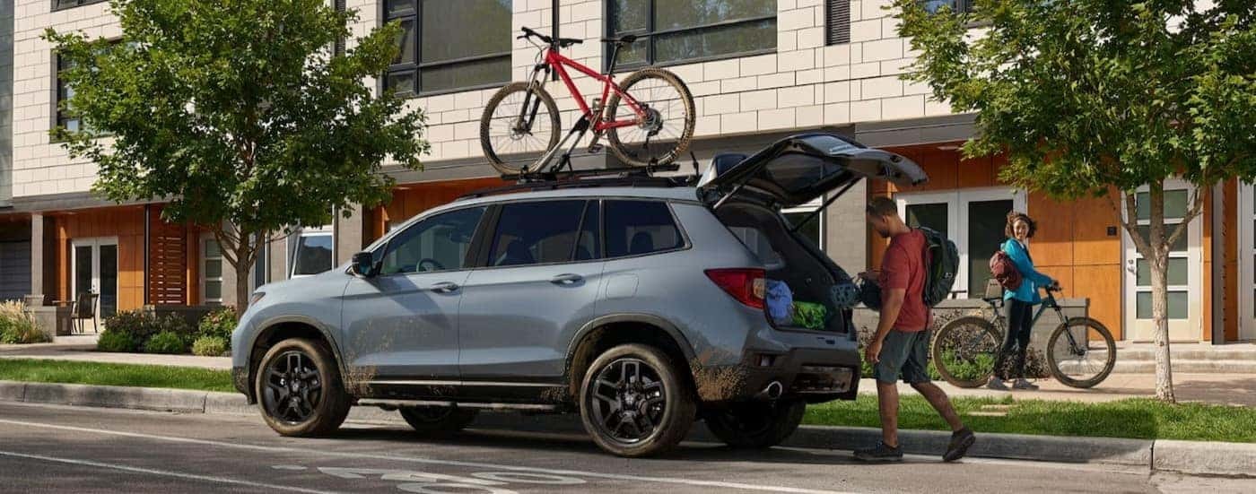 A blue 2024 Honda Passport is shown parked near houses.