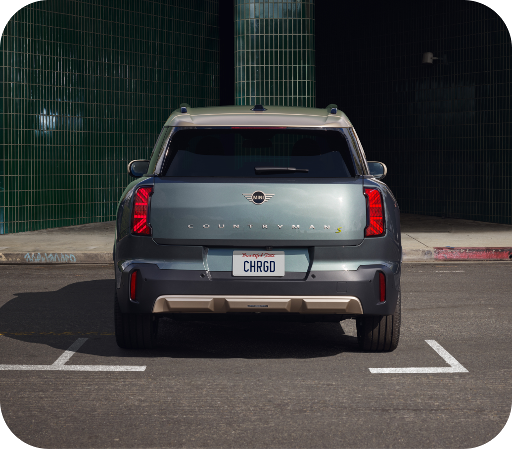 Three-quarters front view of a MINI  Electric vehicle parked on a cobblestone surface in  a parking space in front of a retail storefront in an  urban setting