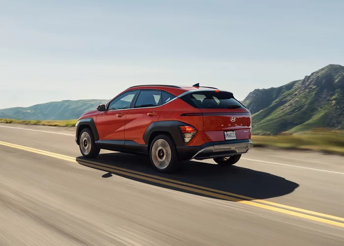 A red Hyundai Kona driving down a road.