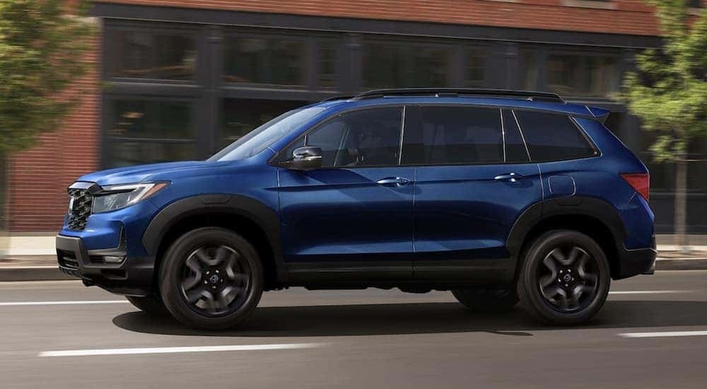 A blue 2020 Honda Passport Elite is shown driving near a building.