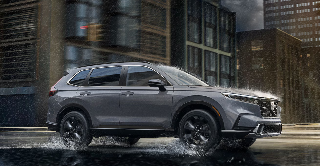 The new 2026 Honda CR-V drives in the rain through a city street.