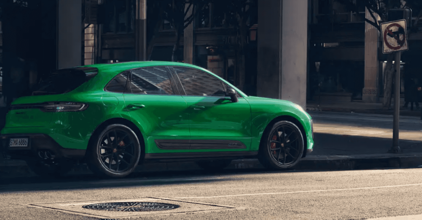 A green Porsche Macan driving in a city.