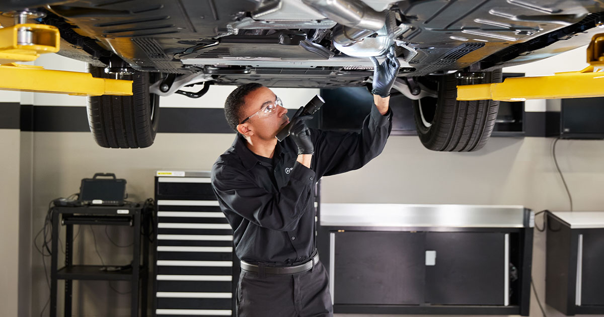 Mercedes-Benz technician works on the underside of a car