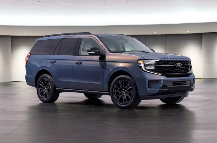 Side three-quarter view of a blue-gray Ford Expedition full-size SUV with black rims parked inside a modern showroom studio.