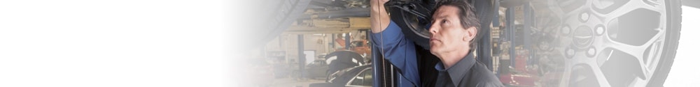 Technician working beside a vehicle wheel in a wide banner image