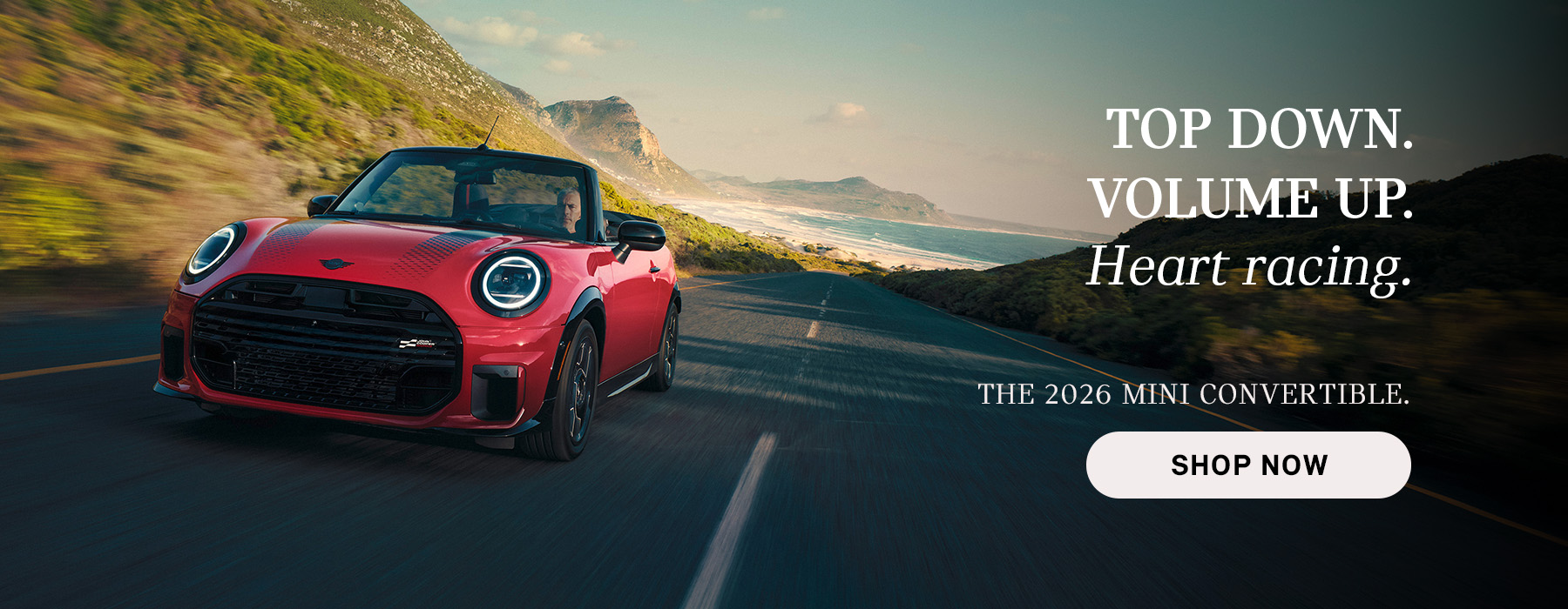 Red MINI convertible driving along a coastal road with mountains and ocean in the background, with advertisement text promoting the 2026 Mini Convertible and a “Shop Now” button.