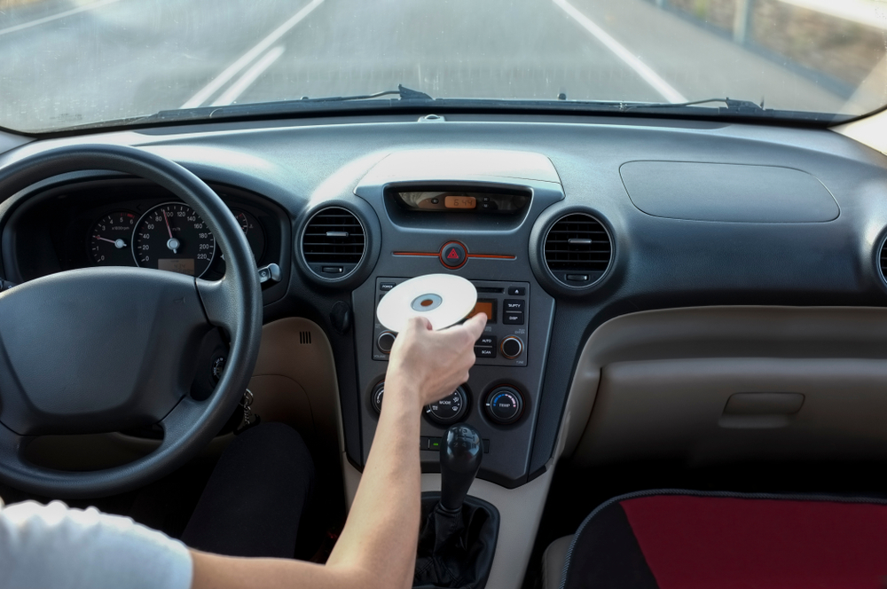 A person’s hand inserting a CD into the CD player of a car, highlighting the process of using a car CD player.